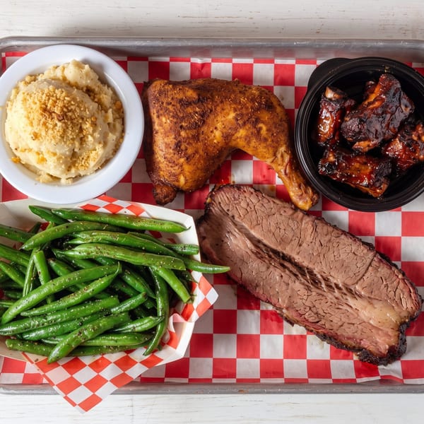 Barbecue platter with chicken, ribs, brisket, mashed potatoes, and green beans on a metal tray.