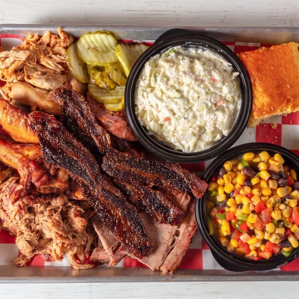 Large barbecue platter featuring pulled pork, brisket, chicken, coleslaw, cornbread, and corn salad.