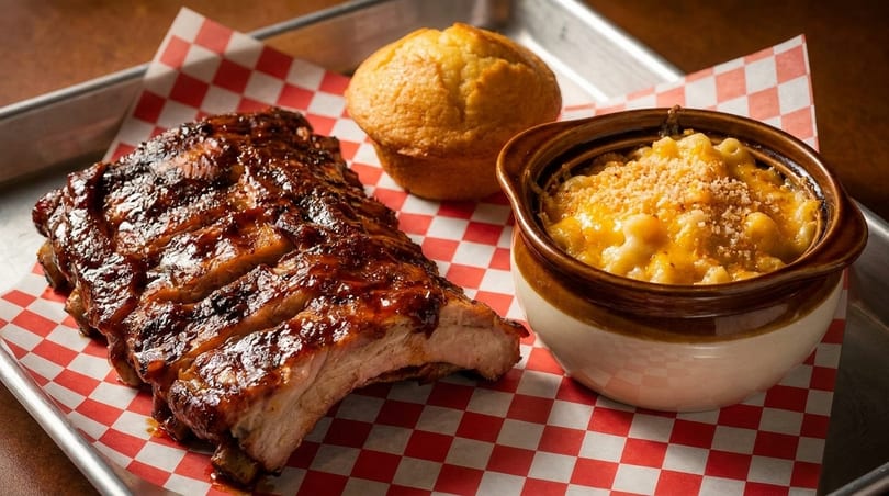 BBQ ribs, mac and cheese, and a corn muffin on a red and white checkered paper.